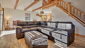 A spacious living room with a large sectional sofa, wooden beams, and a staircase.