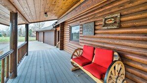 Una baita di legno con un portico in legno, una panca anch'essa in legno e con cuscini rossi, e un quadro con un pesce appeso al muro.