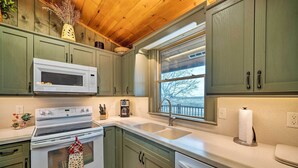 Una cucina con mobili verdi, un forno a microonde bianco, un piano cottura, un lavello e una finestra con vista sugli alberi.