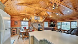 Interno di una baita con soffitto in legno, camino, zona pranzo e un'isola cucina di grandi dimensioni.