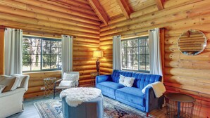 A log cabin interior with a blue sofa, a white armchair, a round table, and a patterned rug. - Log Cabin Retreat with Pool and Vineyard Views (Cottonwood)