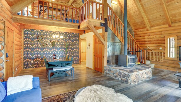 A spacious log cabin interior with a high ceiling, a stone fireplace, a dining area, and a staircase leading to an upper level. - Log Cabin Retreat with Pool and Vineyard Views (Cottonwood)