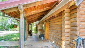 A log cabin with a covered porch, a concrete pathway, and a small outdoor seating area. - Log Cabin Retreat with Pool and Vineyard Views (Cottonwood)
