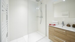 Un baño moderno con cabina de ducha de vidrio, tocador blanco con espejo y un mueble de madera.