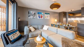 Una sala moderna con un sofá seccional, un sillón pequeño y una zona de comedor con una mesa dispuesta para el desayuno.
