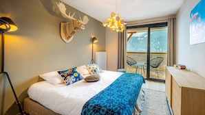 Un dormitorio moderno con cama, cabecera de madera, cabeza de venado montada en la pared, lámpara de pie, lámpara colgante y vistas a un balcón con mobiliario exterior.
