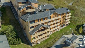 Un edificio de madera de varios pisos con balcones, rodeado de un paisaje cubierto de césped y árboles.