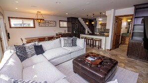 A modern living room with a sectional sofa, a leather ottoman, and a dining area with a wooden table and chairs.