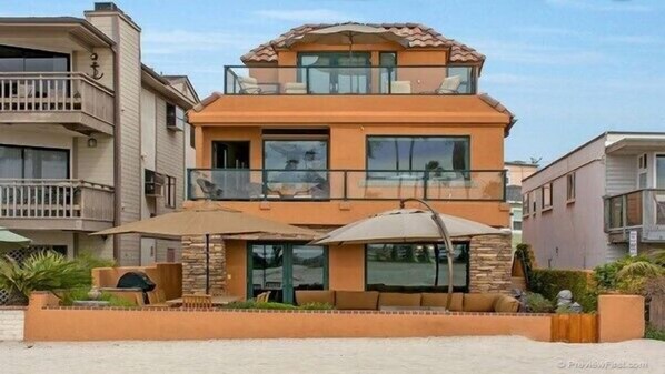 Un immeuble résidentiel de deux étages doté d’un balcon, de grandes fenêtres et d’un patio aménagé avec du mobilier d’extérieur.