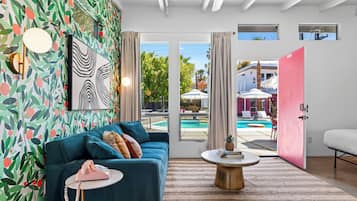 Un salon moderne avec un canapé de couleur turquoise, une table basse ronde et un papier peint aux motifs de feuilles aux couleurs vives.