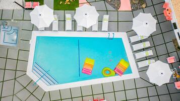 A swimming pool with lounge chairs and umbrellas, surrounded by a tiled deck.