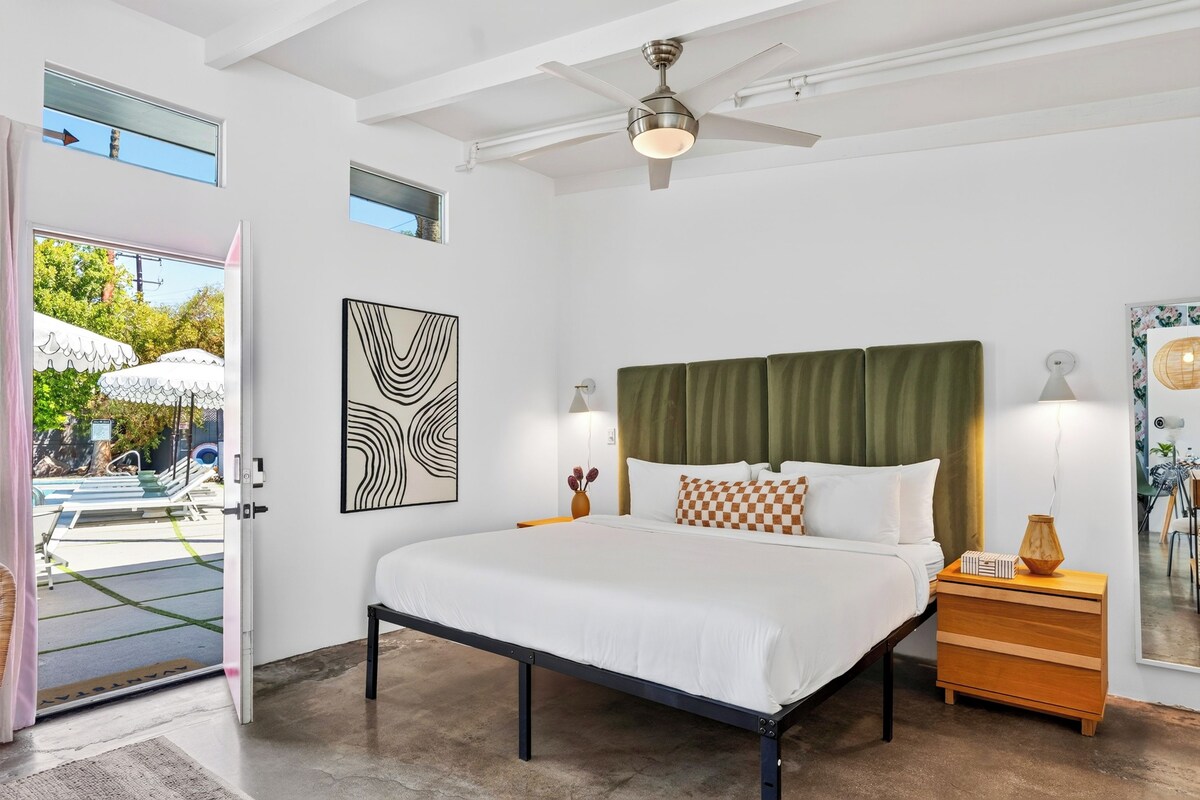 A bedroom with a bed, a nightstand, a ceiling fan, and a view of an outdoor pool area.