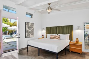 Une chambre avec un lit, une table de chevet, un ventilateur de plafond et une vue sur l’espace extérieur abritant une piscine.