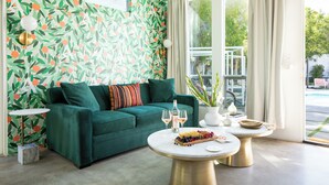 A living room with a green sofa, two round coffee tables, a fruit platter, and a decorative wall with a leafy pattern. - The Wesley by AvantStay (Palm Springs)