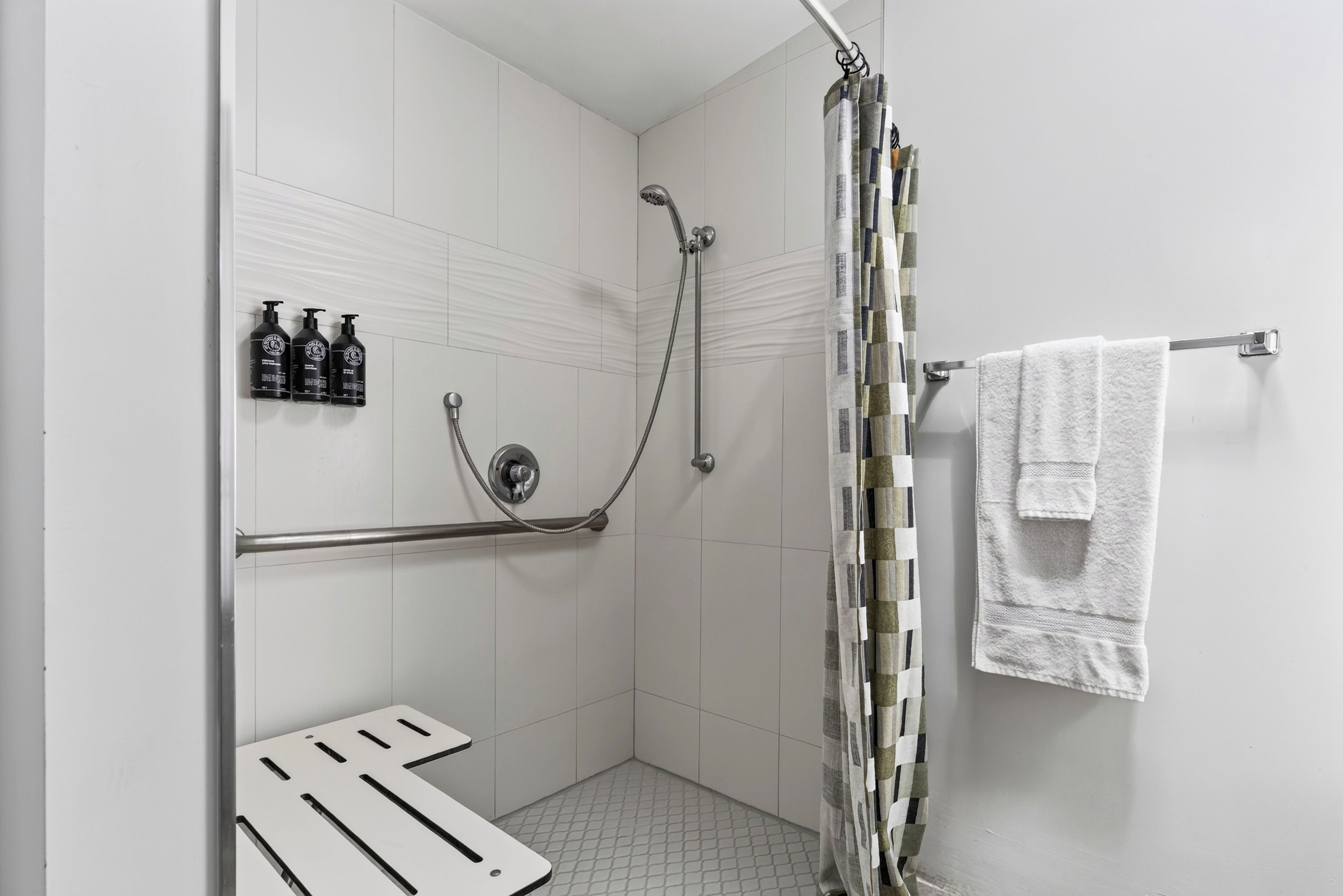 Ein Duschbereich mit Handbrause, einem Handtuchhalter mit einem weißen Handtuch und drei Shampooflaschen an der Wand.