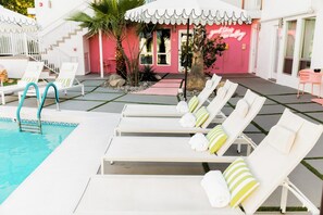 A pool area with lounge chairs, a pool ladder, and a building with a pink facade. - The Rosalie by AvantStay (Palm Springs)