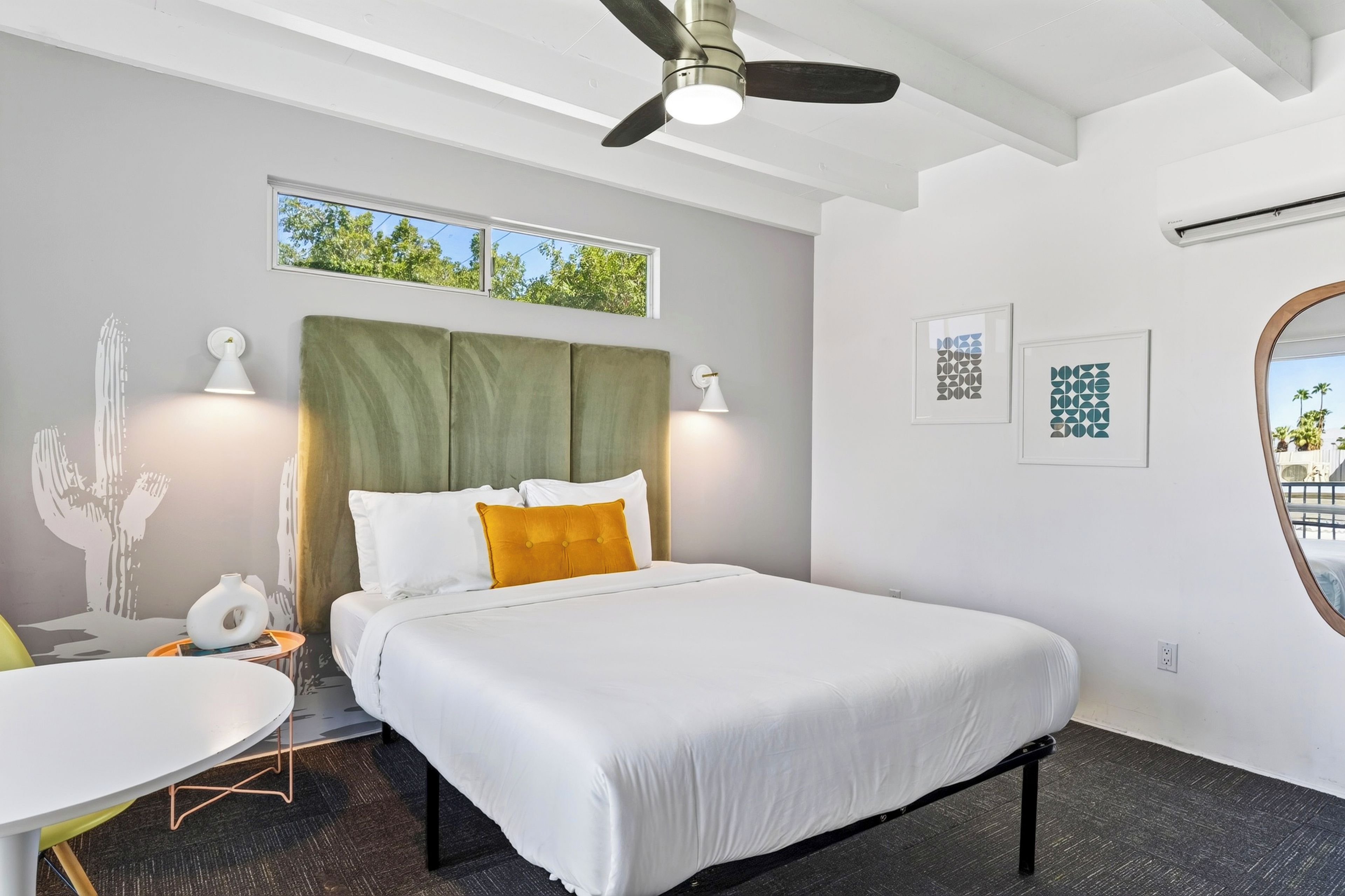 Habitación de hotel con cama, ventilador de techo, ventana y obras de arte en las paredes.