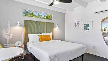 A hotel room with a bed, a ceiling fan, a window, and artwork on the walls.