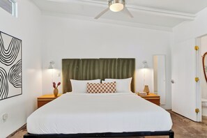 A hotel room with a bed, two bedside tables, a ceiling fan, a large abstract painting, and a mirror. - The Rosalie by AvantStay (Palm Springs)