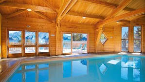 A wooden indoor pool with clear glass doors and windows, reflecting the surrounding scenery.