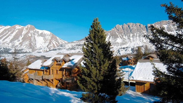 A snow-covered mountain landscape with wooden cabins and a clear blue sky.