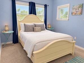 A bedroom with a bed, two bedside tables, a window with curtains, and a wall-mounted picture.
