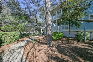 A pathway leading to a building with a balcony, surrounded by trees and shrubs.