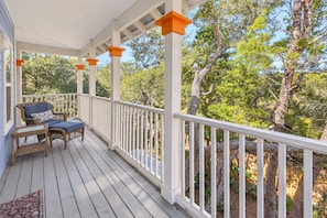A covered porch with a white railing, a wicker chair with a cushion, and a small table. - Good Day Sunshine - 4BR/3BA Old Florida Village Home - Sleeps 8 - Community Pool (Santa Rosa Beach)