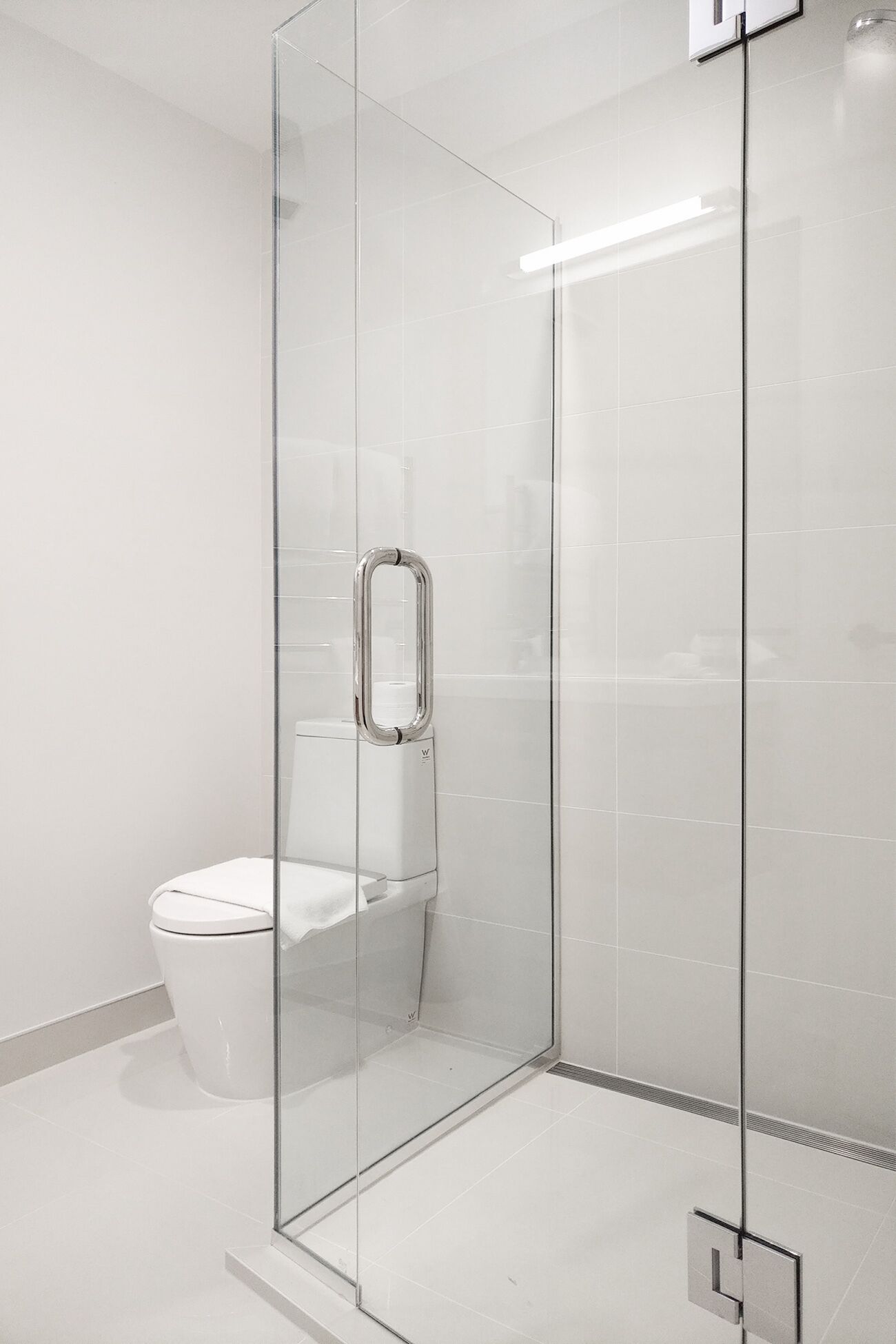 A modern bathroom with a glass-enclosed shower, a white toilet, and a visible water heater.