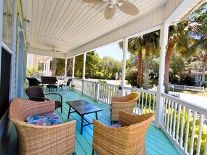 A covered porch with wicker furniture, a table, and a view of the surrounding greenery.