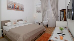 A hotel room with a bed, a TV, a small table with a plant, and a painting on the wall.