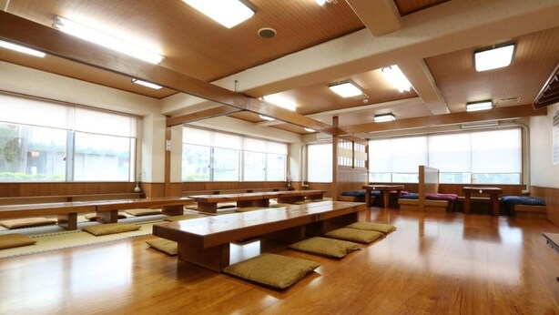 Une pièce spacieuse avec des bancs et des tables en bois, de grandes fenêtres et un plafond en bois.
