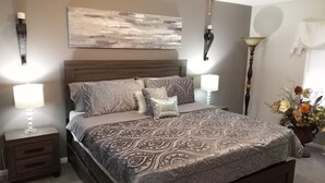A bedroom with a large bed, two bedside tables, a nightstand, a wall-mounted lamp, a ceiling fan, and a painting on the wall. - Spacious home 28 miles from Downtown Chicago (Hammond)