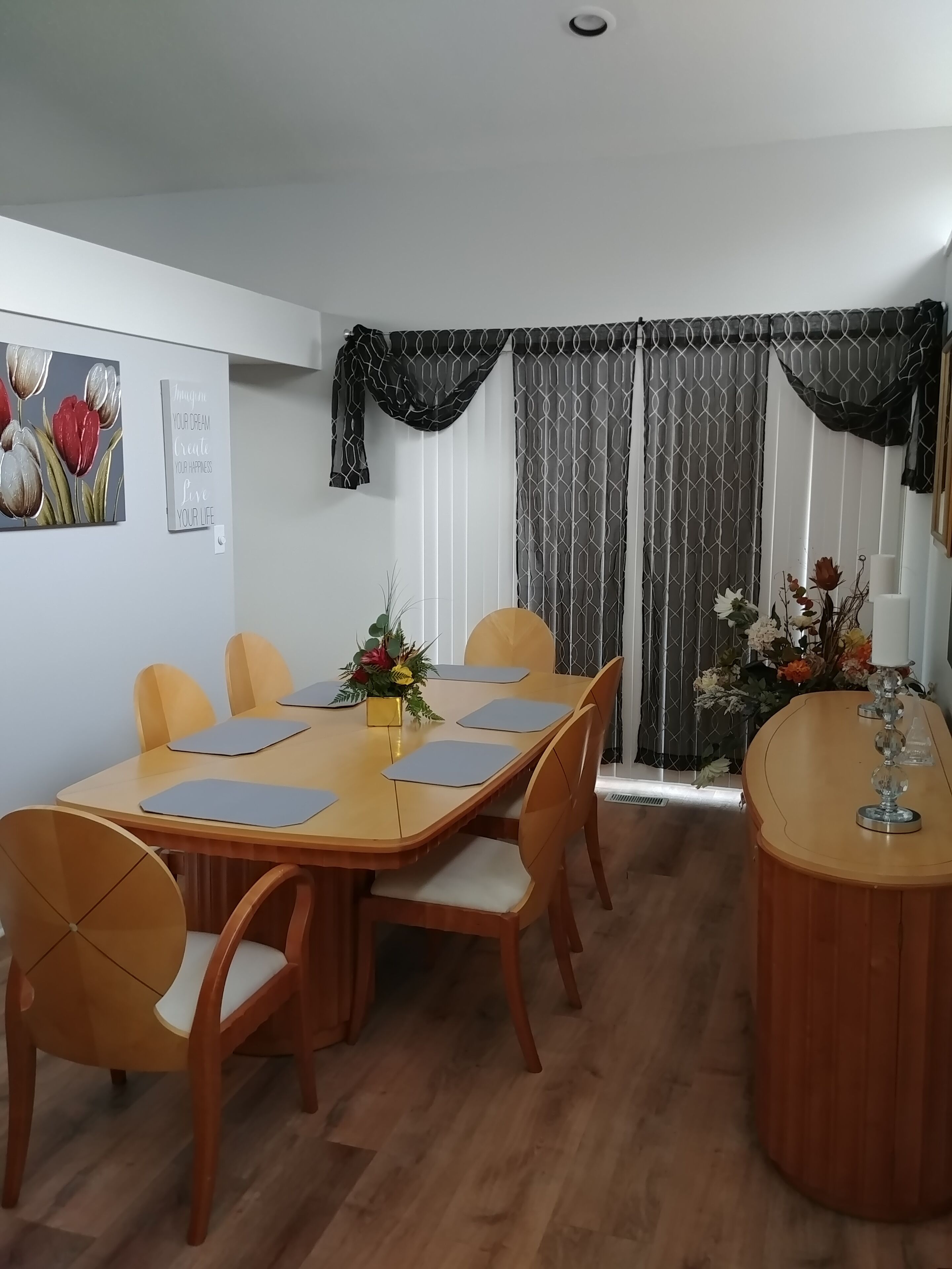 A dining area with a wooden table, chairs, and a vase with flowers.