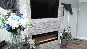A living room with a stone fireplace, a flat-screen TV mounted above it, and a wooden floor. - Spacious home 28 miles from Downtown Chicago (Hammond)