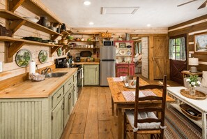A rustic kitchen with wooden cabinetry, a stainless steel refrigerator, and a dining area with a wooden table and chairs. - Romantic Mountain Cottage Near Boone (Purlear)