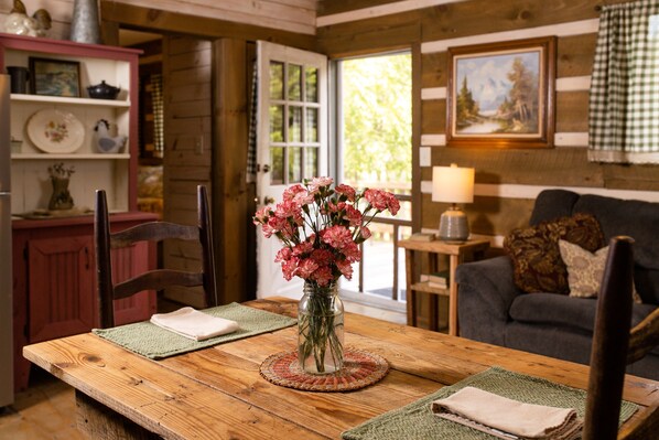 Una mesa de madera para comer con un florero de flores rosas, una lámpara y un mantel a cuadros.
