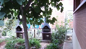 A garden area with two outdoor ovens, a tree, and a brick wall.