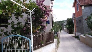A narrow residential street with houses on both sides, a metal gate, and a clear sky.