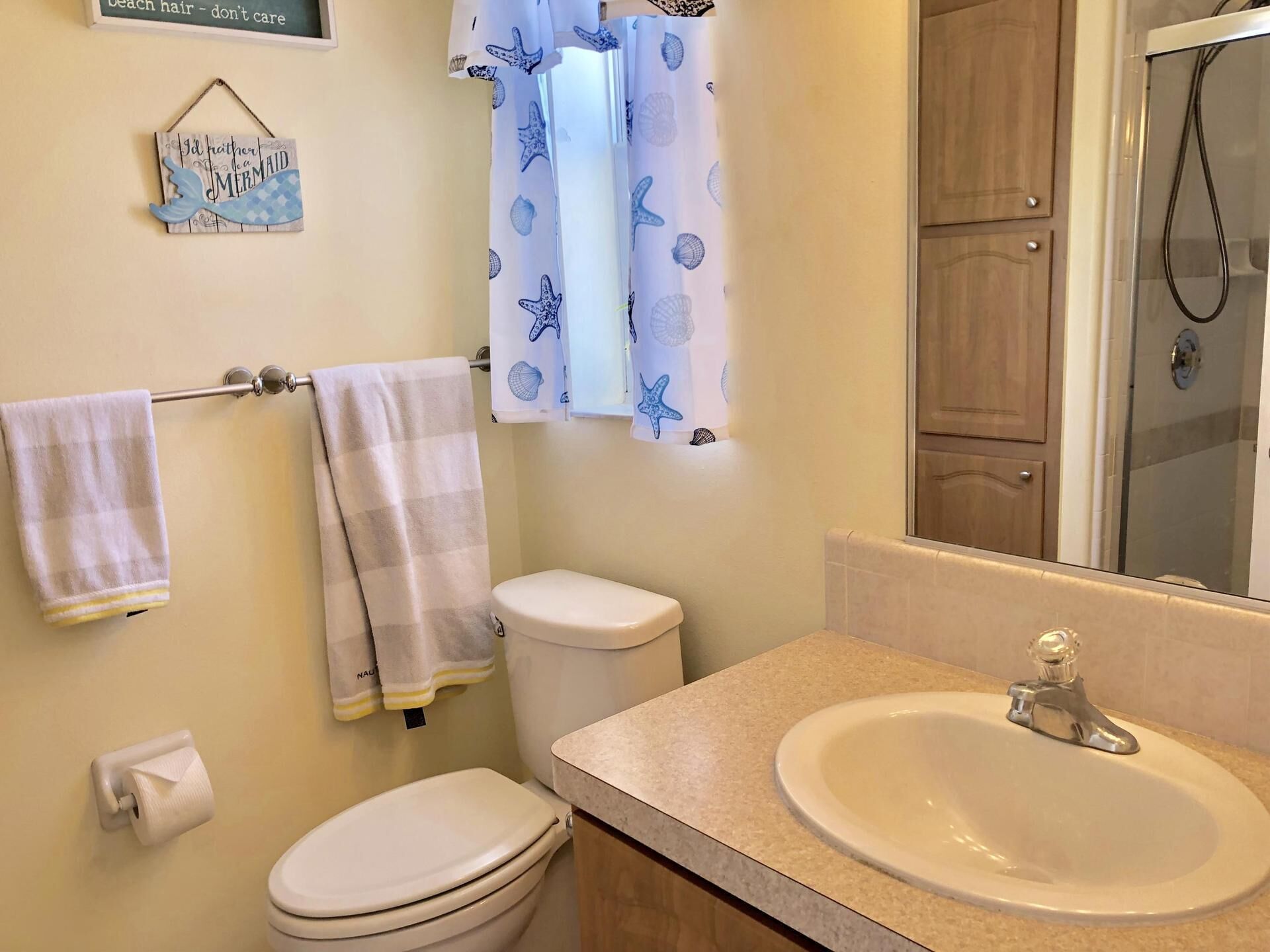 A bathroom with a toilet, sink, and shower. There are towels hanging on a rack and a sign on the wall.