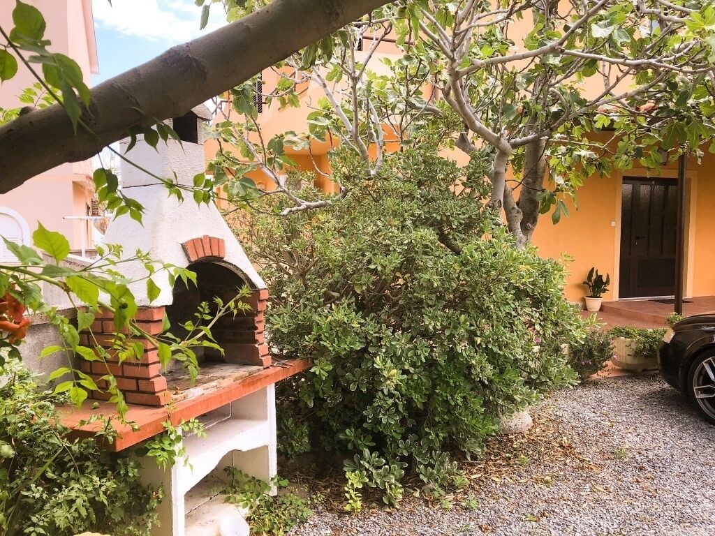 Ein Backofen aus Ziegelsteinen im Freien, ein kleiner Busch und ein Gebäude mit einer Tür im Hintergrund.