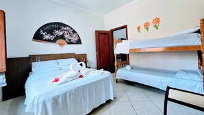 Une chambre d’hôtel avec un lit, un ventilateur, une porte en bois et un mur décoré de motifs floraux.