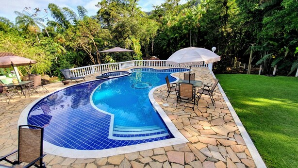 Une piscine au design incurvé, entourée de carreaux de pierre et d’une clôture blanche.