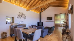 Een gezellige woonkamer met een houten plafond, een eettafel met stoelen, een bank en een televisie aan de muur.