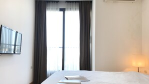 Une chambre d’hôtel équipée d’un lit, d’un téléviseur à écran plat fixé au mur, d’une fenêtre avec des rideaux et d’une lampe de chevet.