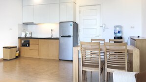 Une cuisine moderne avec des meubles blancs, un réfrigérateur en acier inoxydable et un distributeur d’eau. On y trouve une table à manger avec des chaises en bois et un panier posé sur le sol.