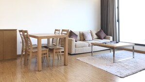 Un salon moderne avec une table à manger en bois, deux chaises, un canapé avec des coussins, une table basse et une grande fenêtre avec des rideaux.