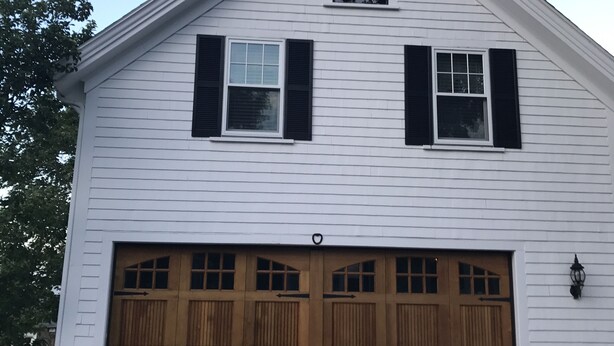 A two-story white house with a garage, wooden shutters, and a small window above the garage.