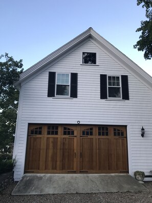 Une maison blanche à deux étages, avec un garage, des volets en bois et une petite fenêtre au-dessus du garage.