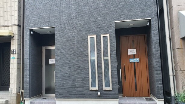 A modern building facade with two vertical windows and a wooden door. - SC1 Kaikanoyado (Osaka)